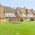 Ferienhaus mit Strohdach und Balkonen auf grünem Grundstück