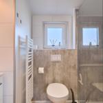 Badezimmer mit Dusche, Toilette und Fenster. Wandverkleidung aus Betonoptik.