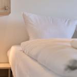 Ein Bett mit weißen Kissen und Bettwäsche neben einem Nachttisch mit Lampe.