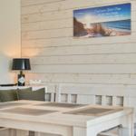 Esszimmer mit Holzwand, Tisch, Stühlen und Wandbild mit Strandmotiv.