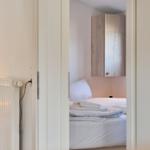 Schlafzimmer mit Bett, Holzschränkchen und Stehlampe.