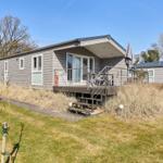 Moderne Ferienhaus mit Terrasse und Garten. Holzverkleidung und Satellitenantenne sichtbar.