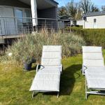 Zwei Liegestühle auf einer grünen Wiese vor einem Ferienhaus.