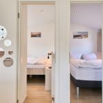 Zwei Schlafzimmer mit Betten und Wandbildern sind über eine Tür mit runden Spiegeln sichtbar.