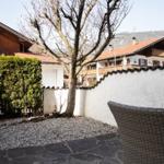Terrasse mit Steinplatten und Gartenbereich mit Kies, umgeben von weißen Mauern und Bäumen.