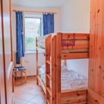Zimmer mit Doppelstockbett, Fenster mit blauen Vorhängen und Holzschrank.