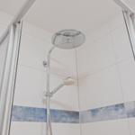 Dusche mit Duschbrause und Handbrause, weiße Fliesen mit blauer Zierleiste.