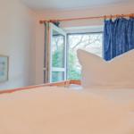 Schlafzimmer mit Bett, Fenster und blauen Vorhängen.