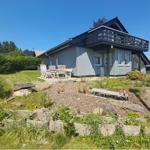 Ein Haus mit Balkon, Garten und Holzmöbel unter blauem Himmel.