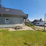 Haus mit Terrasse, Garten und Tisch mit Stühlen. Hintergrund: Straße mit Wohnhäusern.