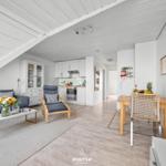 Wohnbereich mit Sofa, Sessel und Küchenbereich. Holzboden und weiße Decke.
