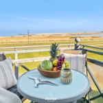 Terrasse mit Tisch, Stühlen und Obstschale. Blick auf Grünfläche und Meer.