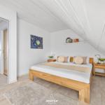 Schlafzimmer mit Holzbett, Nachttischen und Wandbild. Dachschrägen und Holzboden.