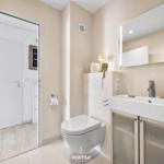 Badezimmer mit Toilette, Waschbecken und Spiegel. Tür führt in einen Flur.