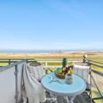 Balcony with table, chairs, and fruit bowl overlooking a grassy area and sea.