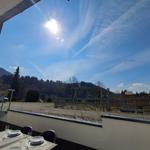Terrasse mit Tisch und Stühlen. Blick auf Wald und Himmel mit Sonne.