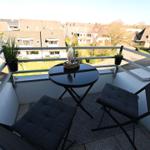 Balcony with table, two chairs, and potted plants overlooking residential area.