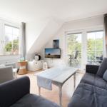 Wohnzimmer mit Sofa, Sessel und TV. Balkon mit Sicht auf Grün.