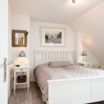 Schlafzimmer mit weißem Bett, Nachttischen und Wandbild unter Dachschrägen.