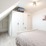 Schlafzimmer mit Dachschrägen, weißem Kleiderschrank und Bett mit gesteppter Bettdecke.