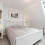 Schlafzimmer mit Dachschräge, großem Bett und Dachfenster. Weiße Einrichtung und Holzboden.