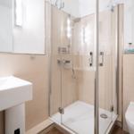 Badezimmer mit Dusche, Waschbecken und Toilette. Wandbild zeigt Strandhaus.
