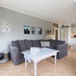 Wohnzimmer mit grauem Sofa, weißem Tisch und Küchenbereich im Hintergrund.