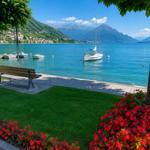 View of lake with boats, benches, and flower beds under trees.