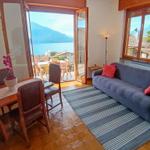 Living and dining area with view of lake and mountains. Sofa, table, and chairs are present.