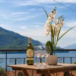 On the terrace, a table with wine, glasses, and an orchid overlooks mountains and lake.