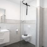 Badezimmer mit Dusche, Toilette und Waschbecken. Glaswand, Spiegel und Fliesen.