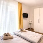 Zwei Betten mit Handtüchern, TV, Kleiderschrank und Fenster mit gelben Vorhängen.