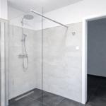 Dusche mit Glaswand, silbernen Armaturen und grauen Fliesen.