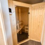 Sauna mit Holzwand, Sitzbänken und Glasfront. Bedienfeld an der Wand.