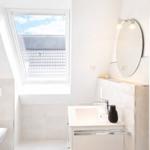 Badezimmer mit Dusche, Waschbecken und Dachfenster mit Blick auf Dach.
