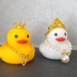 Zwei Schwimmkäfige, ein gelber mit goldenem Herzanhänger und ein weißer mit Perlenkette und Krone.