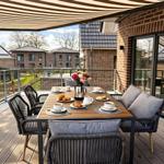 Terrasse mit Esstisch, Stühlen und Sonnenschutz. Blick auf moderne Häuser und Grünflächen.
