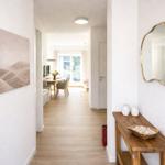 Flur mit Wandbild, Spiegel und Holzbank. Blick in Wohn- und Essbereich.