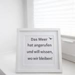 Ein gerahmtes Schild mit Text steht auf einem Fensterbrett. Im Hintergrund sind Jalousien zu sehen.