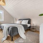 Schlafzimmer mit Bett, Nachttisch, Stuhl und Pflanze an der Wand.