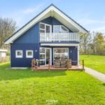 Blau gestrichenes Haus mit Balkon und Terrasse auf grünem Grundstück.