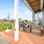 Terrasse mit Sitzgruppe und Tisch unter Holzdecke. Grünfläche und Häuser im Hintergrund.