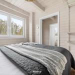 Schlafzimmer mit Bett, Fenster und Holzwand. Blick auf Wald. Kleine Badezimmertür sichtbar.