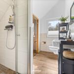 Badezimmer mit Dusche, Toilette und Waschbecken. Holzboden und Fenster mit Blick.