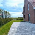 Haus mit gepflastertem Hof, Rasenfläche und Blick auf Felder.
