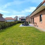Hinterhof mit Rasenfläche, Terrasse und Gartenmöbeln an einer Backsteinmauer.