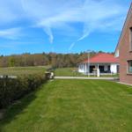 Grüner Rasenbereich mit Blick auf eine weiße Villa mit rotem Dach und Wald im Hintergrund.