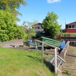 Wooden dock with boat on canal, green trees and red house in background.