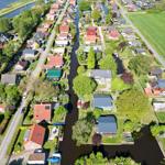Aerial view of a village with houses along a canal and green fields.