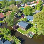 House with boat dock on canal, surrounded by trees and other houses.